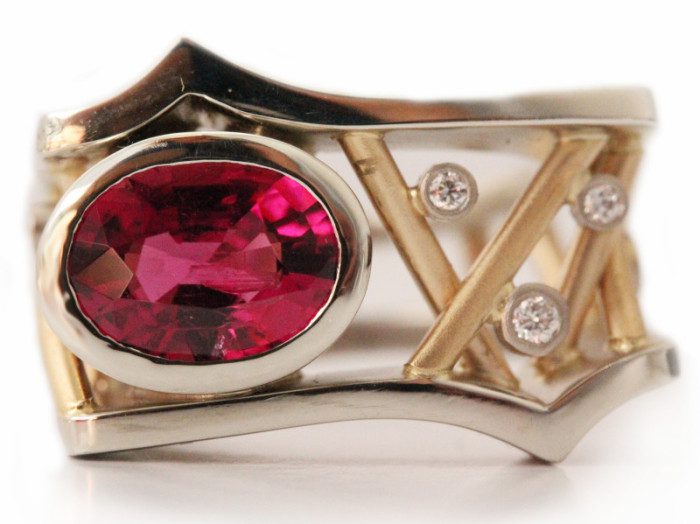 Diamond ring that has an oval ruby gemstone and a bezel round diamond on the bands.