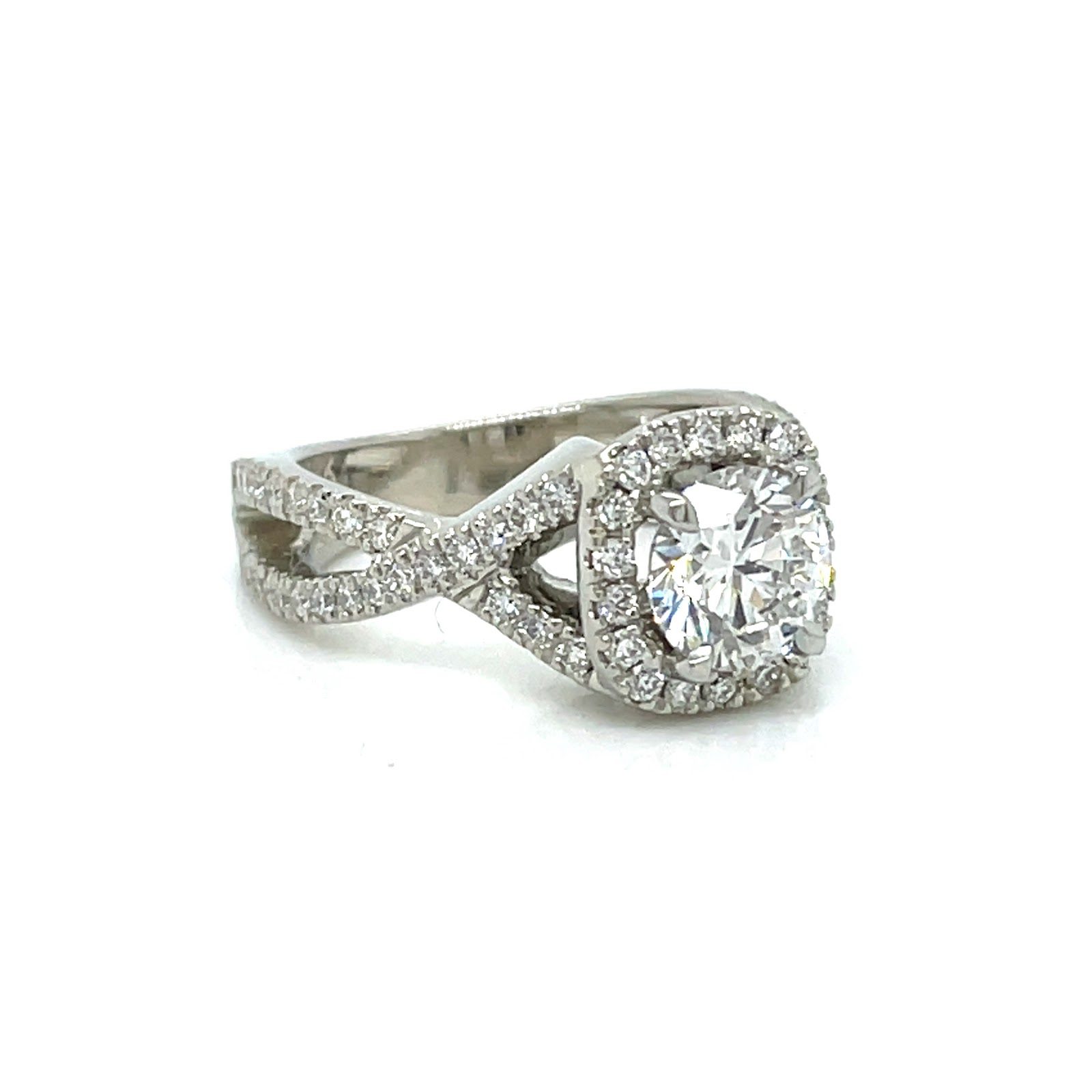 Engagement ring is made of white gold and has a unique band design that resembles two twisted ropes. The band is adorned with small diamonds, and a round diamond is mounted in the center, surrounded by smaller diamonds.